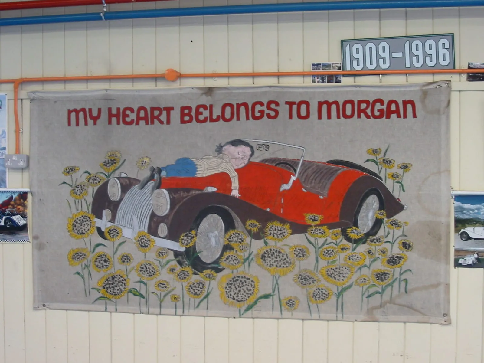 A faded banner on a workshop wall reading “My heart belongs to Morgan”, over a drawing of a red Morgan among sunflowers