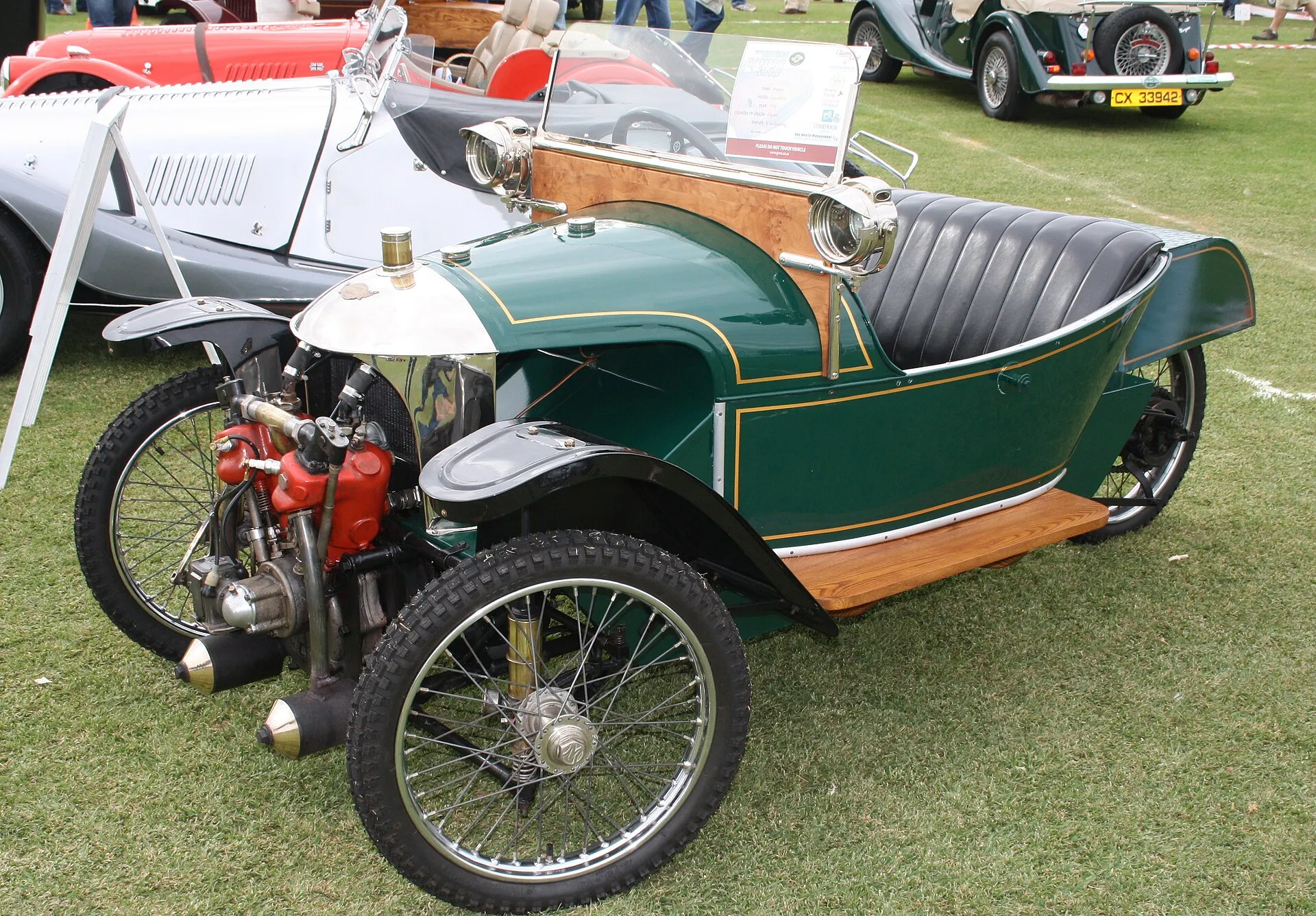 A dark 1918 Morgan Grand Prix three-wheeler on grass, with its exposed V-twin engine