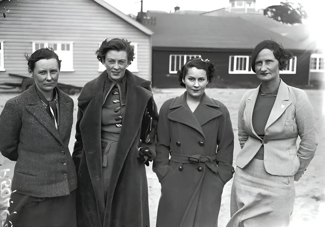 A black-and-white photograph of four women racing drivers standing together beside a building, 1935