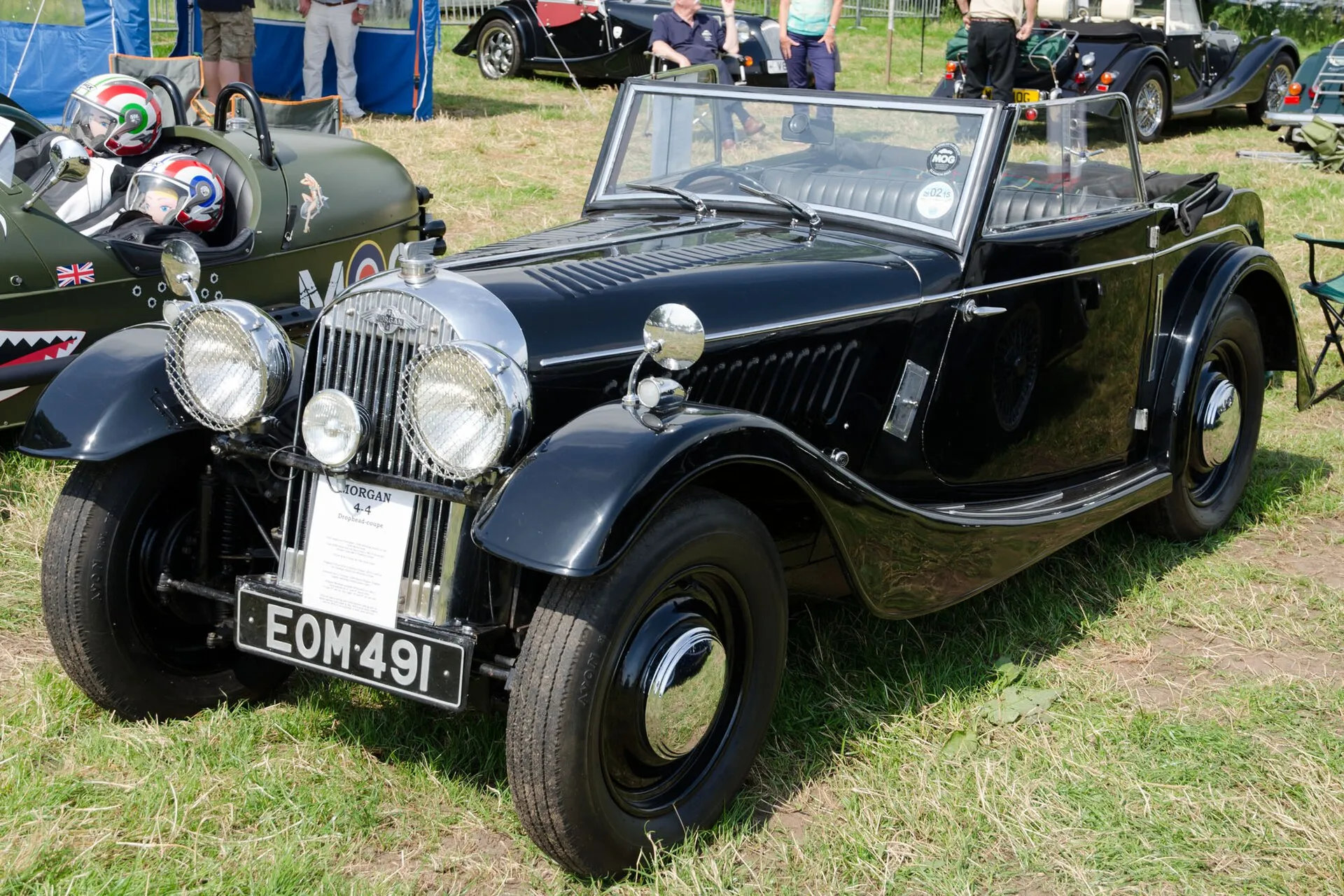 A black 1938 Morgan 4-4 drophead coupé with its hood up, at an outdoor show