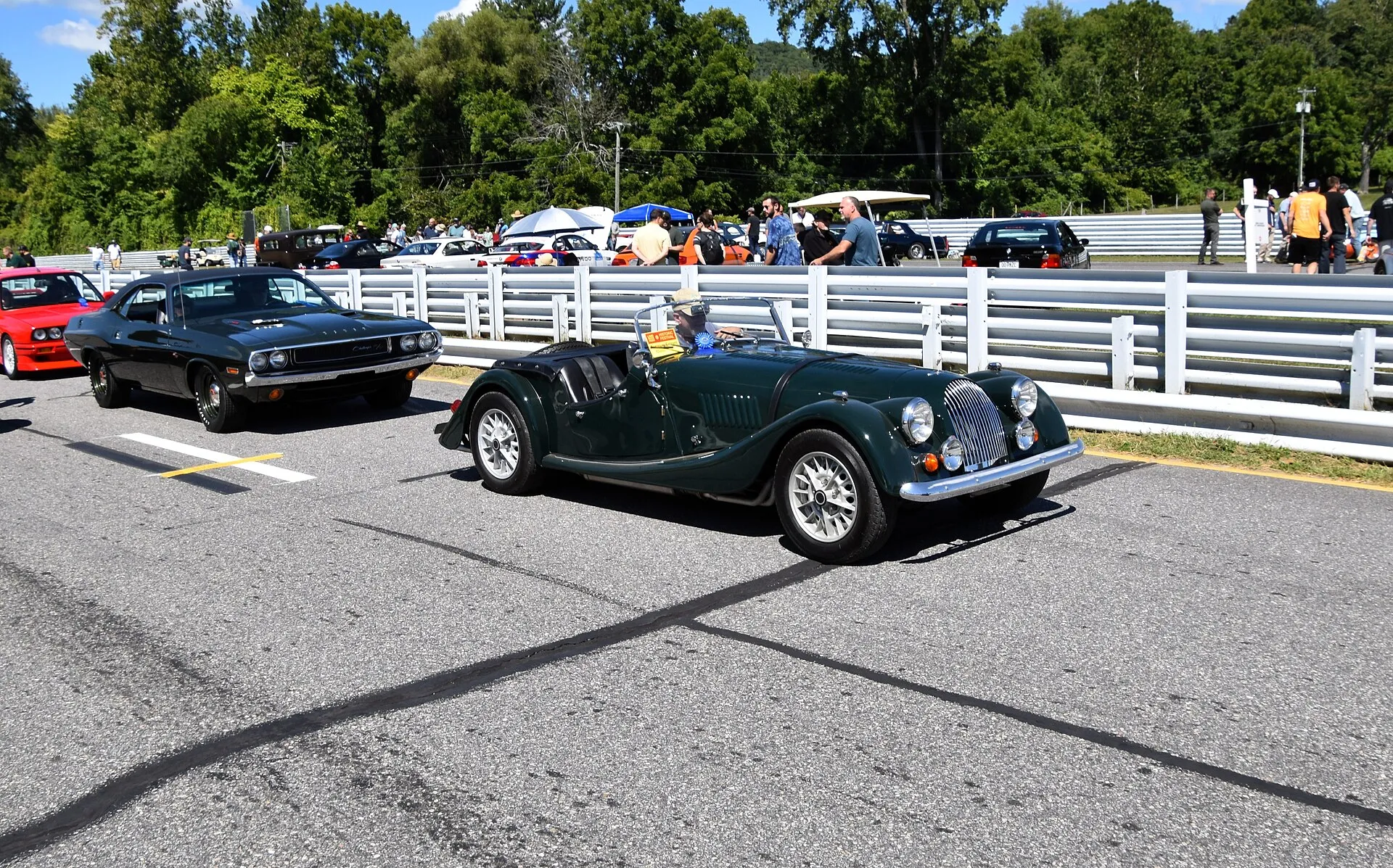 A dark-green 1970 Morgan Plus 8 parked beside a racing circuit fence