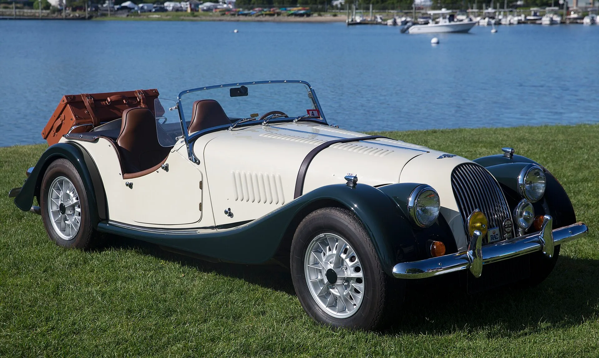 An ivory 1971 Morgan Plus 8 with dark-green wings on a lawn by a harbour