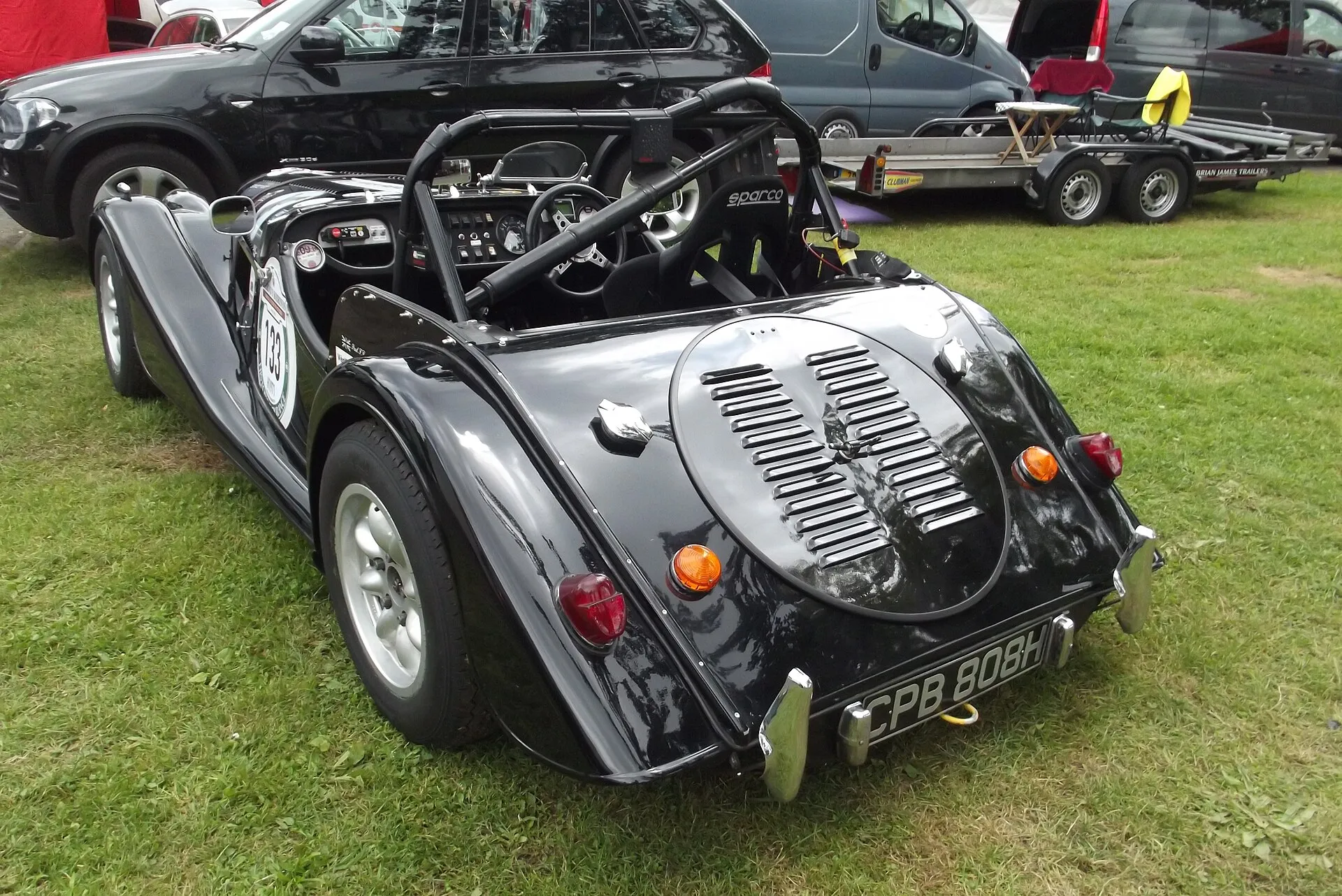 A silver Morgan Plus 8 with alloy wheels, seen from the rear three-quarters, in a paddock