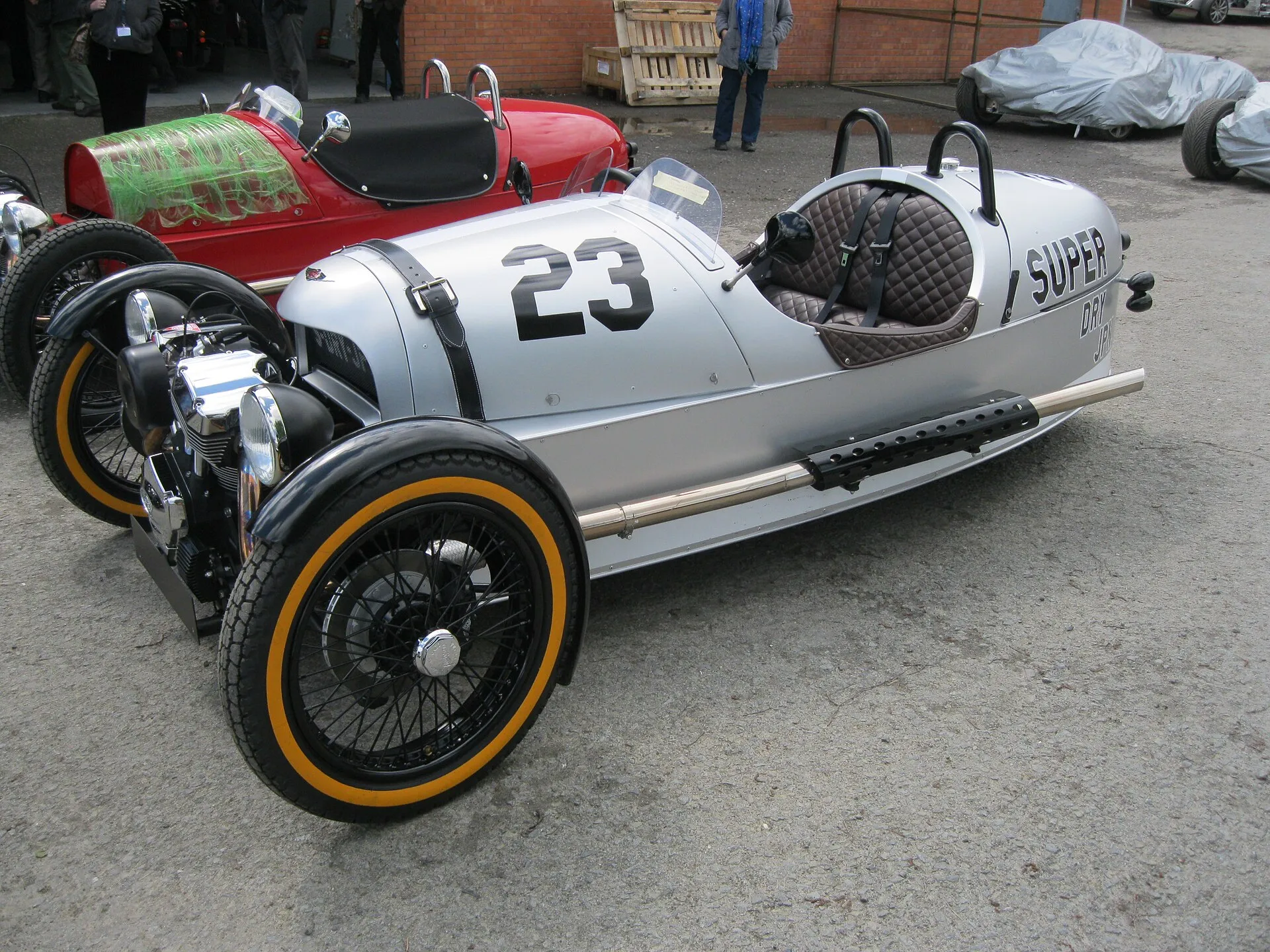 A silver Morgan 3 Wheeler SuperDry edition with race number 23 and orange-walled tyres