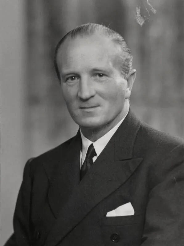 A black-and-white studio portrait of a man in a double-breasted suit and tie, looking slightly to one side