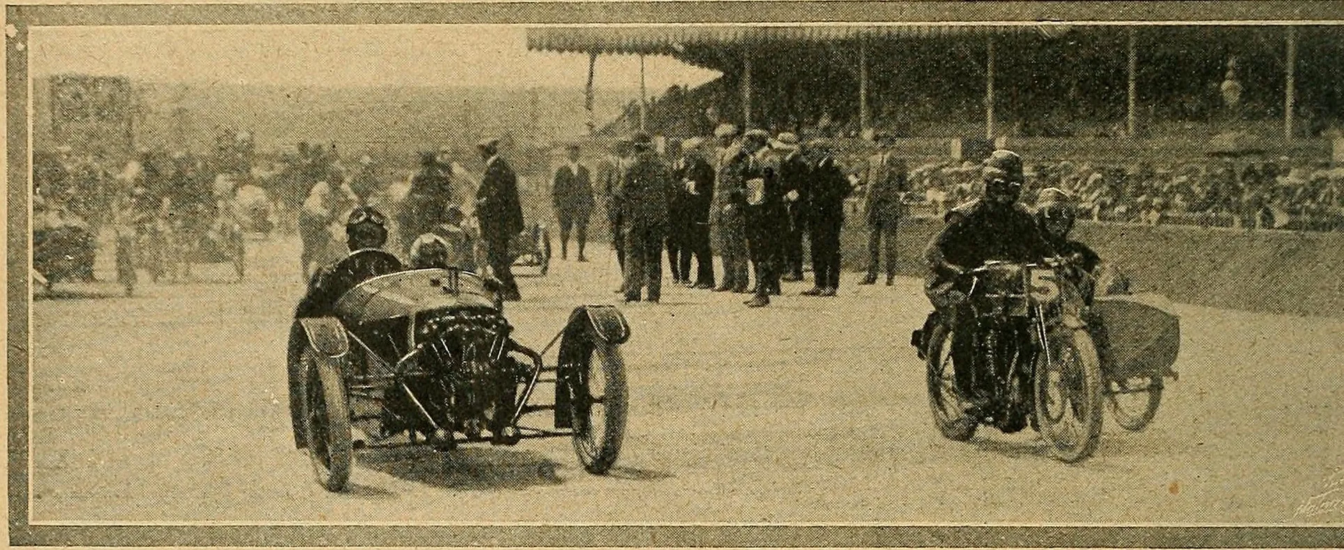 A 1913 photograph of a Morgan three-wheeler with its V-twin engine exposed at the front, driver and passenger aboard, at the start line beside a sidecar motorcycle, with a grandstand and crowd behind